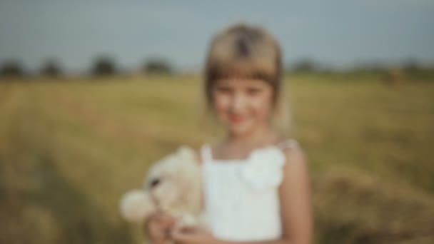 아름 다운 검은 눈을 가진 어린 소녀 비 후는 필드 산책 및 장난감 곰에 의해 재생 됩니다. — 비디오