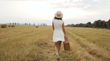 Hasır şapka ve bir çanta ile beyaz bir elbise genç bir kız. Saman ve saman balya. Günbatımı