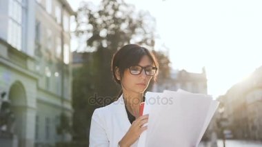 Şehirde yürüyüş ve belgeleri bakarken kahve içme gözlüklü genç iş kadını