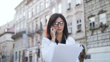 Gözlüklü genç iş kadını ile şehir belgeleri ve telefon görüşmeleri geçer. Dökme kağıt yokuş yukarı sevinçleri
