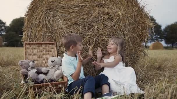 Dvě děti hrají v oblasti pod balíky slámy. Chlapec a dívka bavit chodit v poli. — Stock video