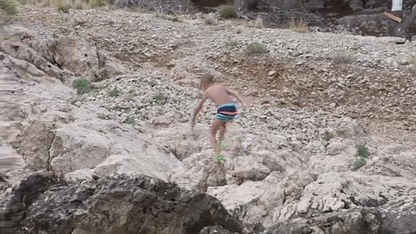 Un hermoso niño caminando en la playa del mar Adriático y escalando alto en la roca arrojando piedras marinas en el agua — Vídeos de Stock