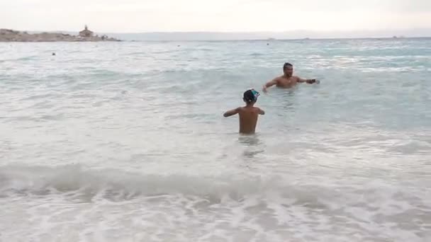 O rapaz com o pai salta nas ondas do mar. Salte com spray de água. Verão dia ensolarado, costa do mar Adriático — Vídeo de Stock