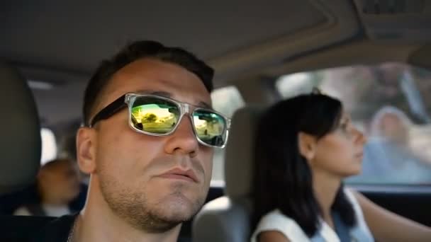 A young woman driving a car. A young man wearing sunglasses goes in a car with his wife and has fun tricks — Stock Video