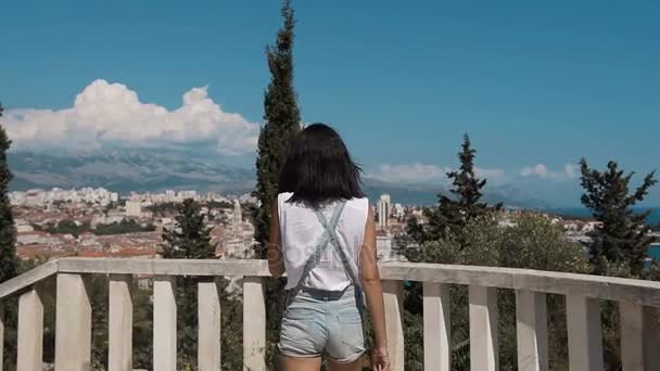 Mladá žena v džínách, stojící na alejí parku s výhledem na město — Stock video