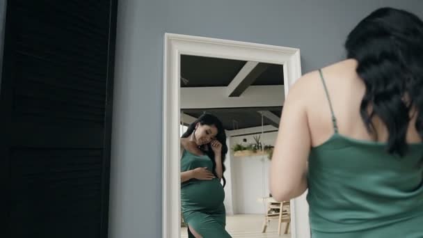 Uma mulher grávida vestida com um vestido de noite verde é exibida em um espelho . — Vídeo de Stock