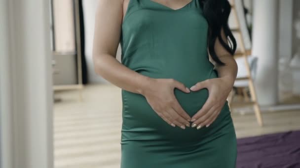 Gros plan des mains des femmes fait coeur sur le ventre, mis en évidence sur une robe verte. Le concept de soins de santé . — Video