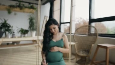 Genç güzel hamile kız uzun saçlı ve ahşap bir patlama sallanan ve kameraya bakıyor güzel küpe.