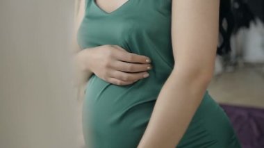 Hamile bir kadın babys midesini sallıyor. Yeşil giysili bir hamile kadın