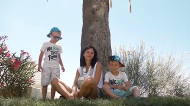 Genç anne ve küçük oğulları, palmiye ağaçları altında oturan ve yakıcı güneşten gizleme var eğlenceli. Eğlenceli tatil