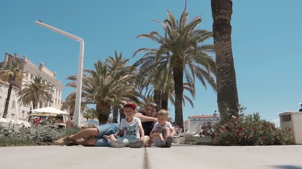 Une bonne jeune famille est assise sur le sol sur le front de mer de la ville split et amusant fait une photo de famille — Video