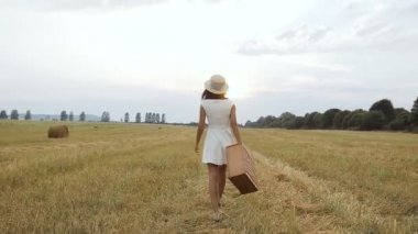 Alan. Gün batımı. Genç bir kız olan bir hasır şapka ve bir bavul alana gider.