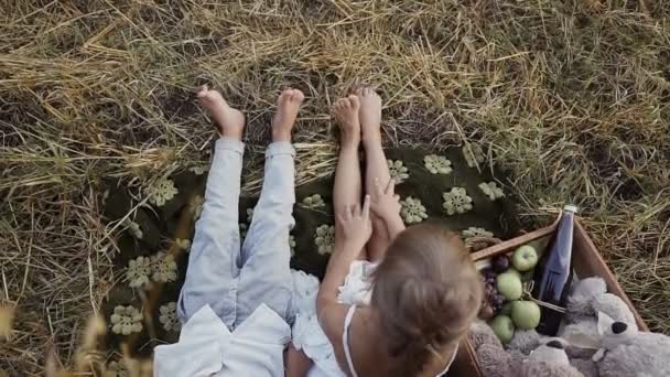 Két fiatal gyerekek ülnek egy mező alatt a csupasz lábak Szalma bála. Egy fiú egy lány eszik gyümölcsöt — Stock videók