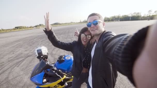 Twee vrienden motorrijders jonge kerel en jong meisje dragen van een zonnebril doen sephi bij zonsondergang in de buurt van een motorfiets — Stockvideo