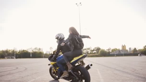 Jovem bela família motociclista ao pôr-do-sol equitação em sua moto. Roupas de couro, mochila, jeans — Vídeo de Stock