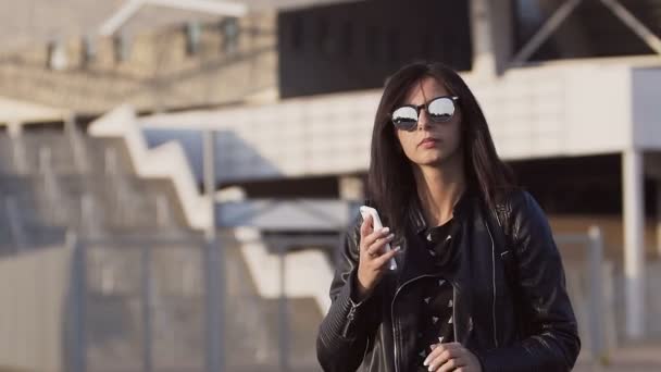 Una mujer de negocios hermosa y elegante sonríe hablando por teléfono fuera del edificio de oficinas — Vídeo de stock