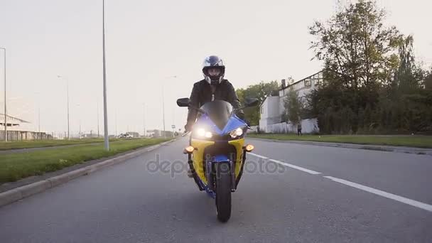 Un jeune motard vêtu d'une veste en cuir et un casque chevauchant la moto le long de l'autoroute autour de la ville. Gros plan — Video