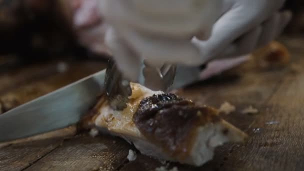 Повар с ножом и вилкой. Профессиональный повар в ресторане или отеле готовит или режет запечённую свинью — стоковое видео