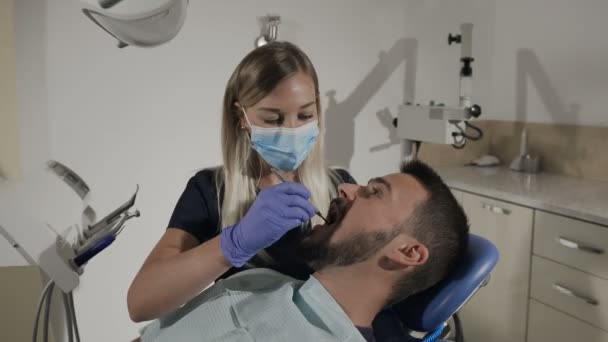 Dentista femenina examinando los dientes del paciente con un espejo bucal y una excavadora dental — Vídeos de Stock