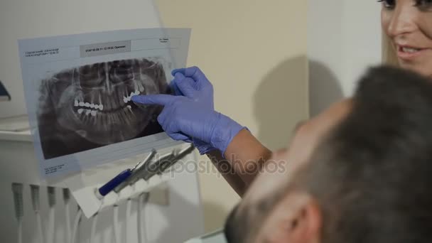Die Zahnärztin zeigt der Patientin ein Röntgenbild zur weiteren Behandlung der Zähne. Zahnmedizin. Zahnarzt zeigt jungen Mann kranken Zahn auf Röntgenbild — Stockvideo