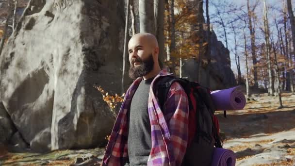 Um jovem bonito com barba caminha no dia quente do outono. Um turista viajou na floresta na temporada de outono. Pedras nas montanhas — Vídeo de Stock