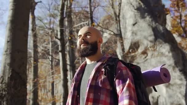 Um belo jovem barbudo vestindo uma camisa em uma gaiola está caminhando alegremente ao longo do caminho da floresta . — Vídeo de Stock