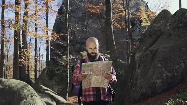 Un hipter maravilloso con barba, parado en lo alto de las montañas y sosteniendo una tarjeta turística en sus manos. Concepto de turismo de otoño — Vídeo de stock