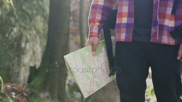 Un turista vestido con jeans negros y una camisa en una jaula va por el bosque y tiene un mapa de turismo — Vídeo de stock