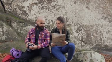 Bir kamera, bir turist kartı ve genç bir kızla bir kayaya oturan ve gün batımında çekim bir sırt çantası ile seyahat genç fotoğrafçı