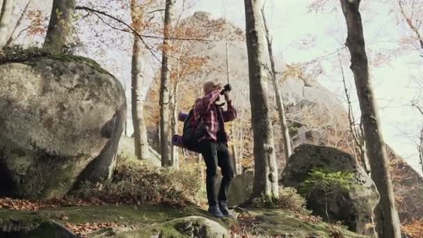 Стильний молодий бородатий чоловік фотографує скелі високо в горах в осінній сонячний день — стокове відео