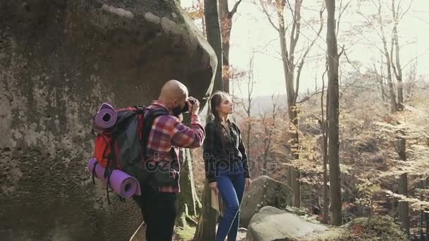 Des hipsters dans les montagnes. Un jeune homme photographe photographiant une belle fille aux cheveux longs tressés dans une tresse. Automne chaude journée ensoleillée — Video