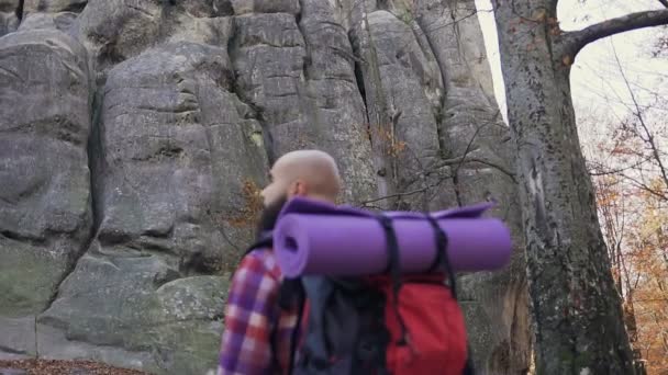 Le magnifique hipster portant une barbe est haut dans la montagne et tient un sac à dos sur les épaules. Le concept de tourisme d'automne — Video