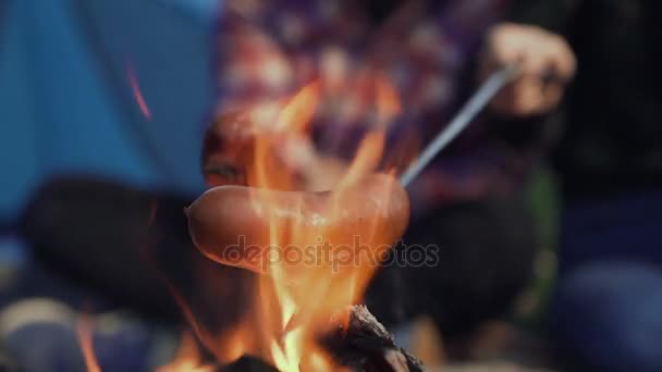 소시지 구이 캠핑, 캠프 파이어 이상의 소시지를 굽고. 관광객은 불꽃 근처에 앉아 — 비디오