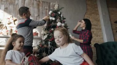 Yakın çekim. Mutlu anne Noel ağacı süslemeleri ve onların İkiz kızları oyuncak ata binmek. Happy New Year ve Noel