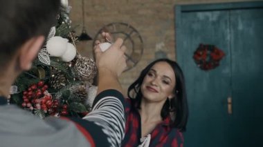 Güzel genç kız neşeyle onun erkek arkadaşına gülümsüyor ve ona bir Noel ağacı süslemek için Noel dekorasyonları verdi. Mutlu yeni yıl ve mutlu Noeller