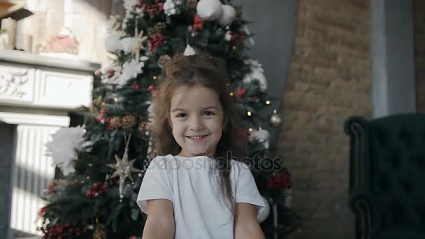 Niña hermosa de pie cerca de un árbol de Navidad y sosteniendo un regalo de Navidad en la caja — Vídeos de Stock