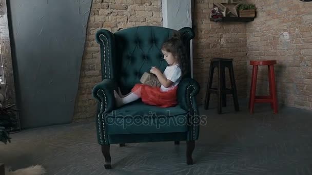 Adorable girl opening present box of gifts sitting on the chair in living room with Christmas tree — Stock Video