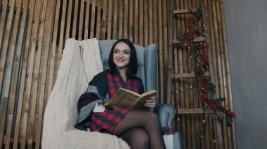 Mutlu küçük çocuklara kitap elinde tutuyor ve çelenk ile dekore edilmiş duvar yanındaki sandalyeye oturur onların sevgi anne kucaklar. Mutlu Noeller ve mutlu bir yeni yıl