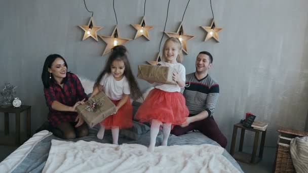 Glad familj sitter på sängen och kastar sina julklappar — Stockvideo