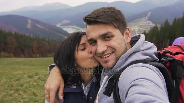 클로즈업입니다. 젊은 여자는 뺨에 부드럽게 남편을 키스. 젊은 가족 재미는 화창한가 날에 산악 지역에서 야외에서 휴식 — 비디오