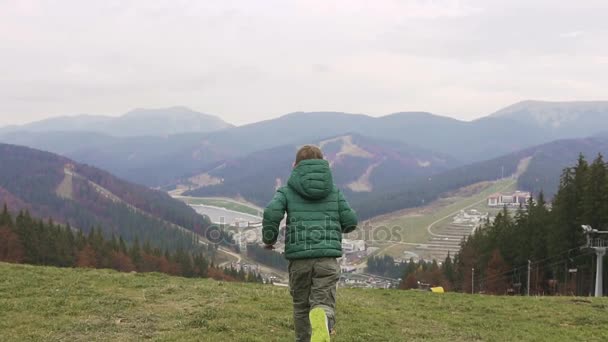 Yeşil bir elbise ile yüksek dağdan aşağı çalışan bir çocuk. Sunny sonbahar günü Bukovel — Stok video
