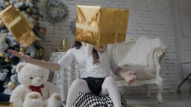 Una mujer joven con un niño pequeño se sienta en un piso cerca de un árbol de Navidad en una habitación espaciosa y luminosa y se regocija en regalos en cajas de oro. Blanco el oso de juguete se sienta en el suelo cerca del árbol de Navidad — Vídeos de Stock