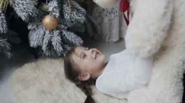 Kapat-up.The çekici kız bir yumuşak beyaz halı üzerinde yatıyor ve bir büyük Peluş ayı ile oynanır. Kış tatili. Noel ağacı