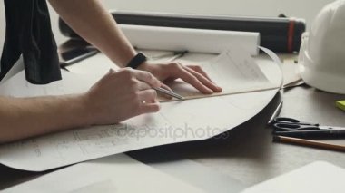 Genç bir erkek mimar yeni daire projesi üzerinde çalışıyor. Koca bir mimar bir plan, grafik, tasarım, geometrik figürler bir kalem ile ofis masasında büyük kağıda berabere olduğunu