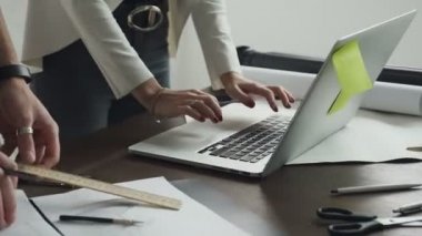 Kadın ve dizüstü ve masaüstü yalan beyaz kağıt sayfalarının çizilmiş yeni projeler üzerinde çalışan erkeğin elinde close-up. Mimarlar proje