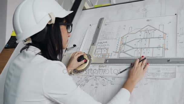 En närbild av en kvinnlig arkitekt som har hjälm och glasögon arbetar med ett projekt i ett bostadshus — Stockvideo