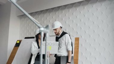 Beyaz zor kask içinde güzel genç Mimarlar klasör tartışırken fikirler çizim ve ofiste çalışırken gülümseyen bir dizüstü bilgisayar ve kağıt kullanıyorsanız