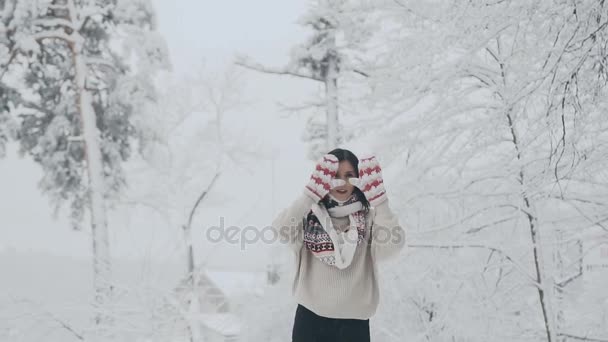 Krásná žena na sobě teplé zimní svetr a šátek, skrývá její oči rukama v palčáky, těší zasněžené zimní den v přírodě