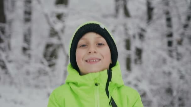 Primo piano di un ragazzino che indossa una giacca verde chiaro e un cappello in un giorno d'inverno lancia palle di neve. Un bambino in una foresta invernale — Video Stock