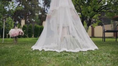 Yakın çekim uzun gelin düğün kader. Bir özel evin avlusunda bir sıcak yaz gününde adımlar yeşil çimlerin çalışır uzun beyaz bir örtü ile gelin tarafından alınır